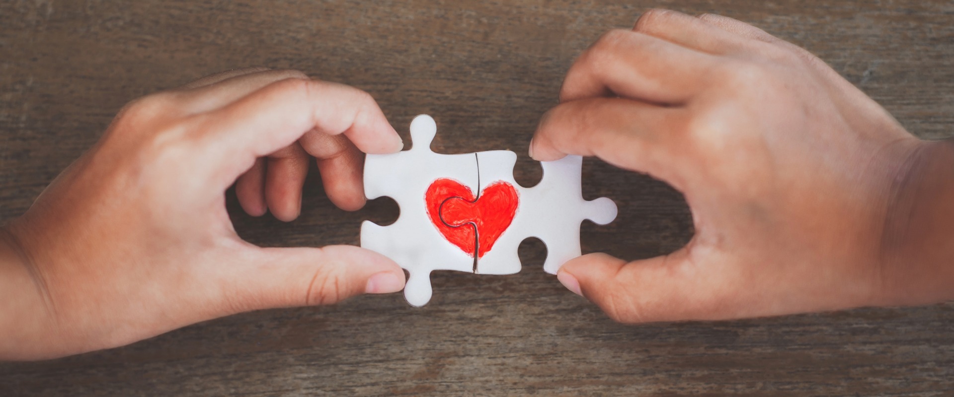 Two hands holding together white puzzle pieces featuring a red heart, symbolizing the interconnected elements of heart health and overall wellness.