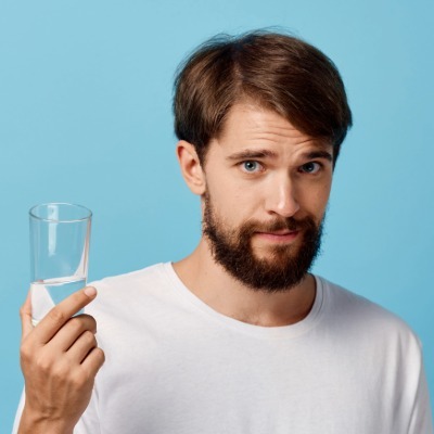 Man holding a glass of drinking water with a thoughtful expression, representing consumer questions about pharmaceuticals in drinking water.