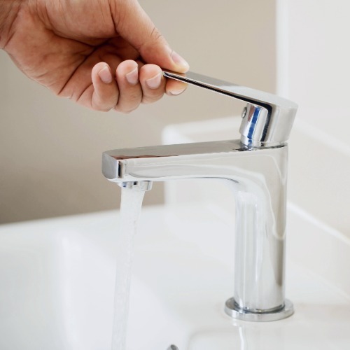 Hand turning off a running faucet to conserve water at home