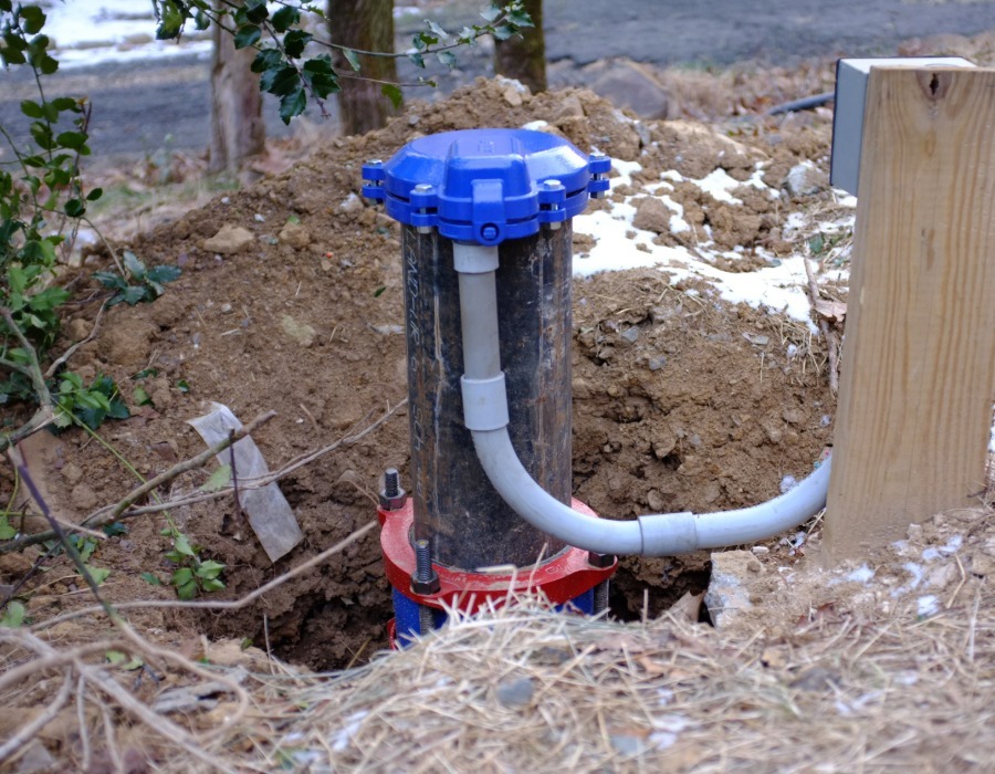 Private water well with exposed plumbing and piping surrounded by disturbed soil.