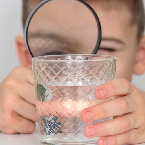 Child examining a glass of drinking water with a magnifying glass.